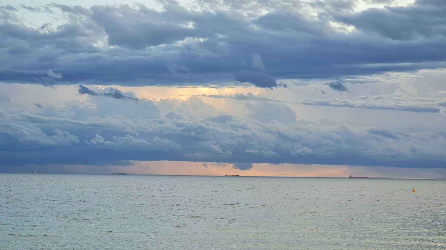 A moody stormy sunset with soft yellows and blues over an ocean shore art