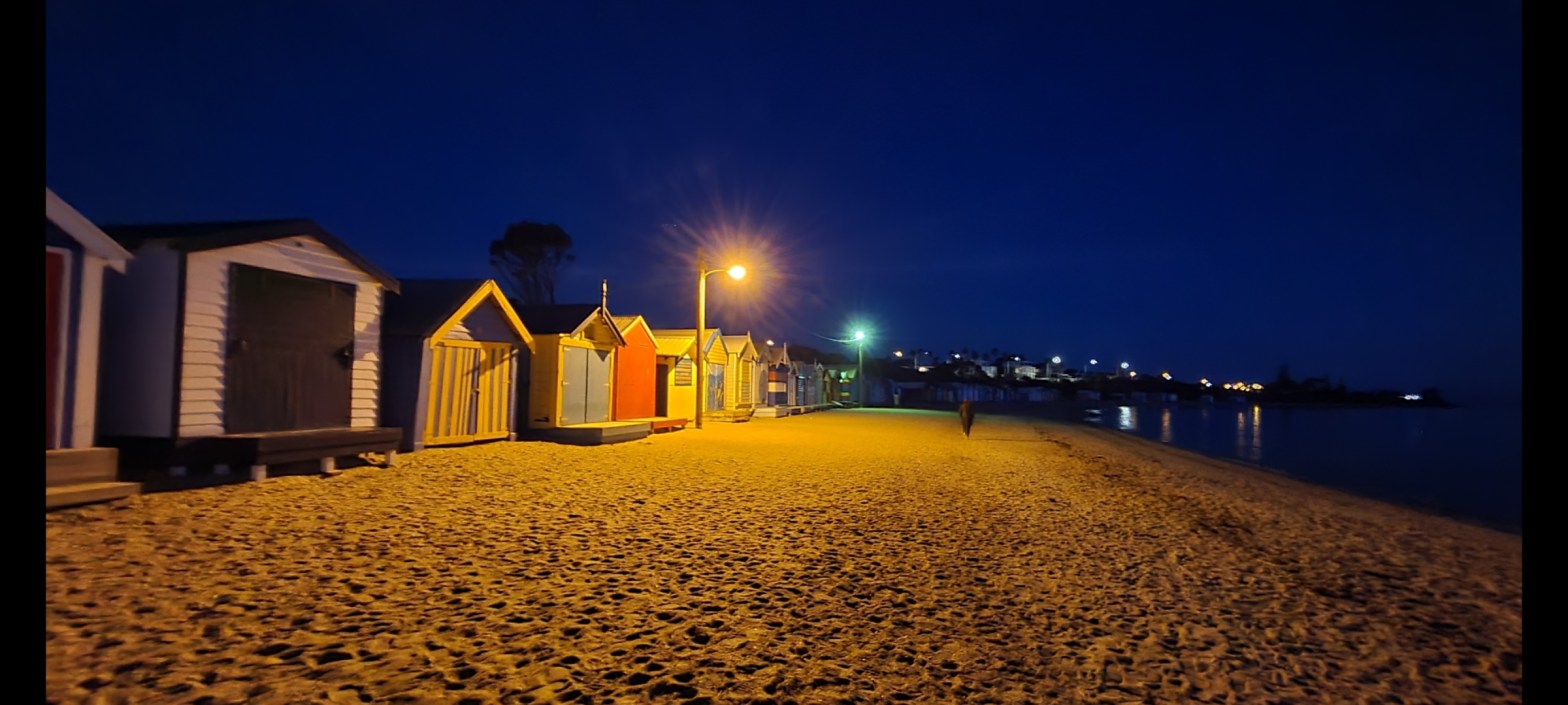 A mystical series of beach houses after dusk lit by orange lamps